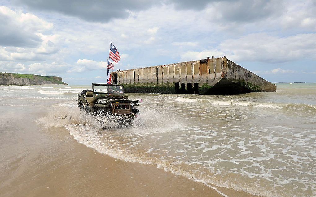 Een als militair verklede Fransman rijdt in een Amerikaanse jeep over het strand bij Arromanches-les-Bains. beeld AFP