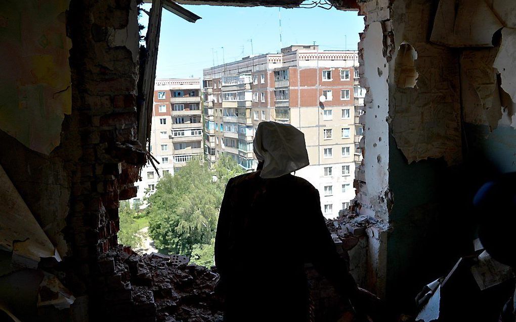 Een vrouw kijkt vanuit haar zwaarbeschadigde appartement in Kramatorsk naar buiten. Beeld EPA