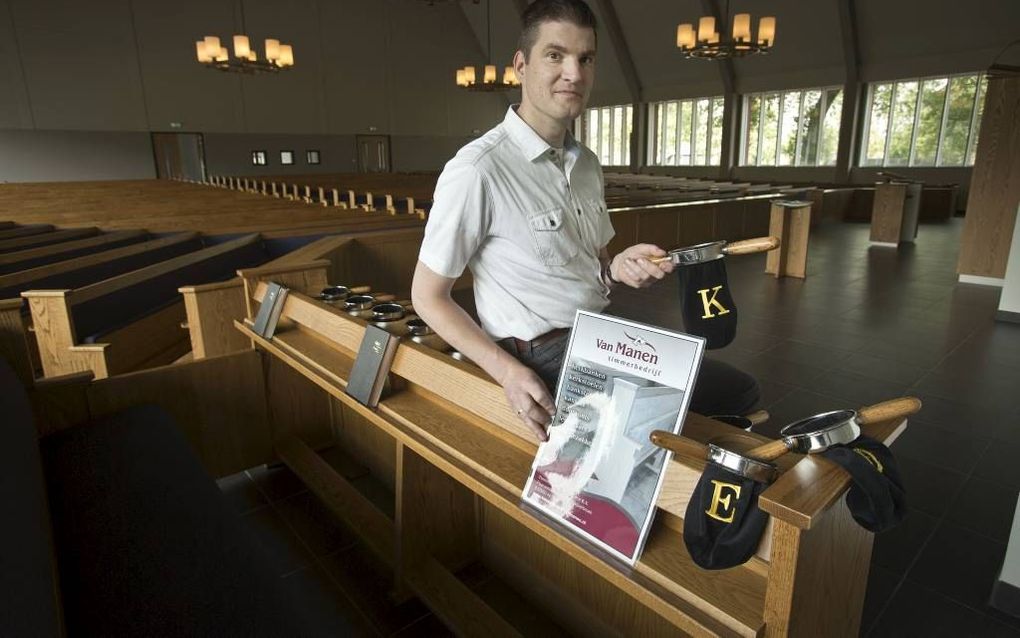 EDE. Henk Donkersteeg voor het rek met collectezakken in de kerk van de gereformeerde gemeente te Ede. „Zo vind ik het het mooist: het collecterek met de zakken aan de bank van de diakenen. Maar dat lukt natuurlijk niet altijd.” Beeld RD, Henk Visscher