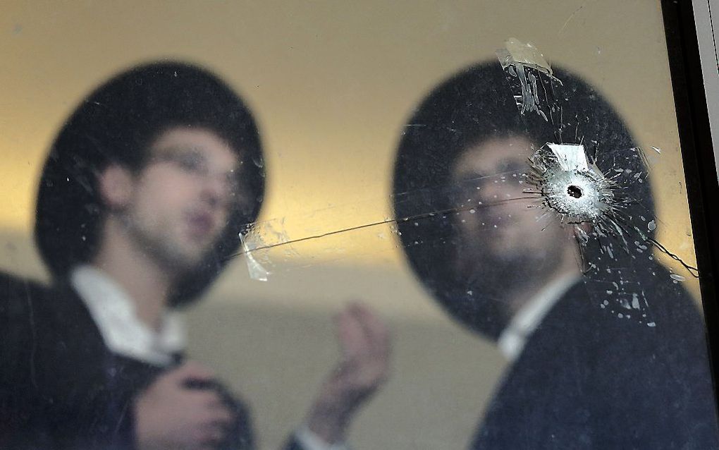 Twee mannen kijken naar kogelgaten in een raam van de getroffen synagoge in Jeruzalem. Beeld AFP