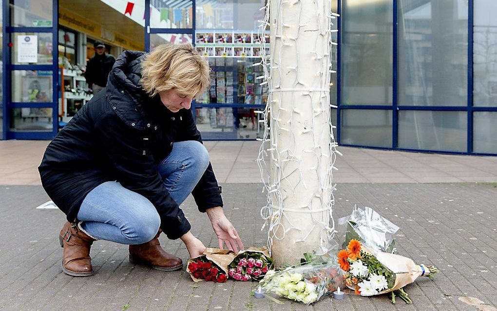 Een vrouw legt bloemen op de plek waar een straatmuzikant werd neergestoken voor de deur van een supermarkt in Zwolle. Beeld ANP