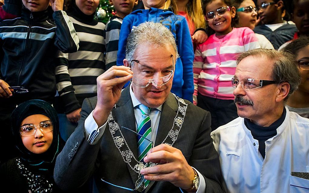 Burgemeester Ahmed Aboutaleb (M) reikt dinsdag, samen met oogarts Tjeerd de Faber, de eerste vuurwerkbrillen uit aan leerlingen van de Talmaschool uit Rotterdam, tijdens de lancering van de Oud & Nieuw Campagne. Beeld ANP