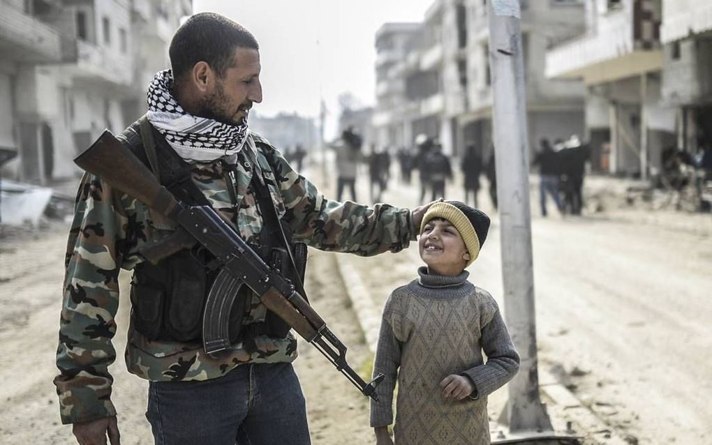 Een Koerdische strijder loopt met zijn kind in de stad Kobani, waar na vijf maanden IS verdreven lijkt te zijn. Dat is tegelijkertijd ook het enige echte militaire succes waarop de anti-IS-coalitie vooralsnog op kan bogen. beeld AFP