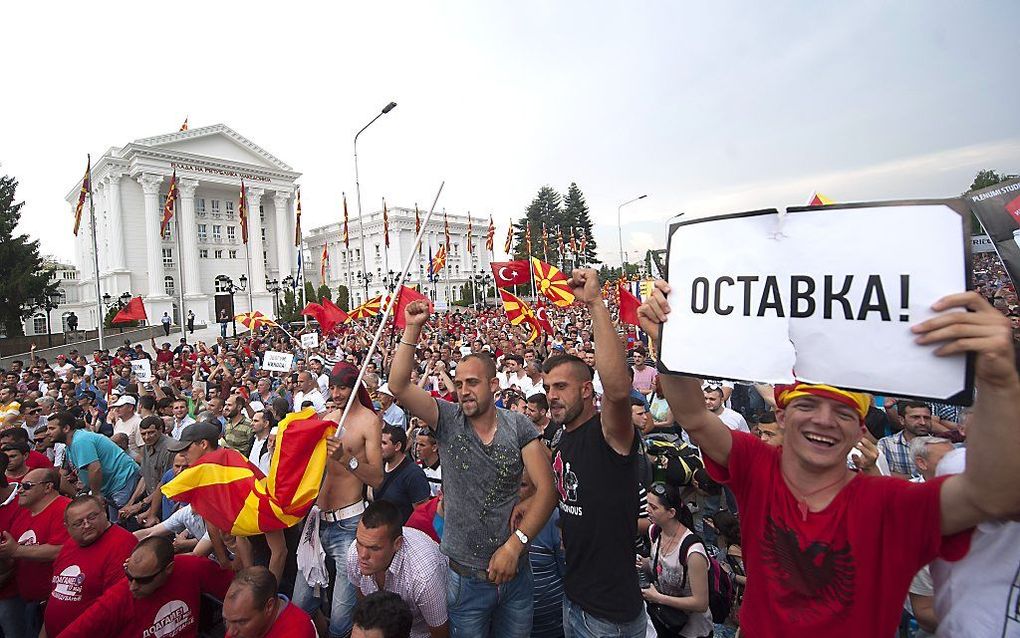 Een man houdt een bordje met de tekst 'Aftreden' omhoog tijdens een protest voor het parlementsgebouw in Skopje. Beeld AFP