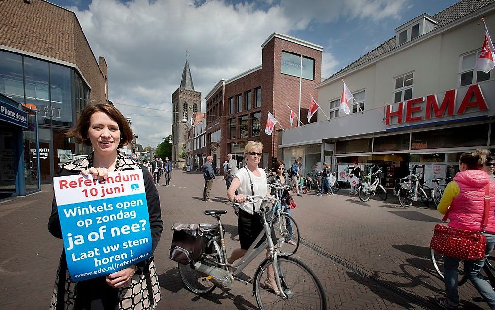 EDE. Gemeentevoorlichtster Judith Wind met de poster van het referendum over de koopzondag in de winkelstraat van Ede-centrum. Op de achtergrond de Oude Kerk van Ede. „Hoe meer inwoners van onze gemeente op 10 juni stemmen, hoe beter dat is voor een repre