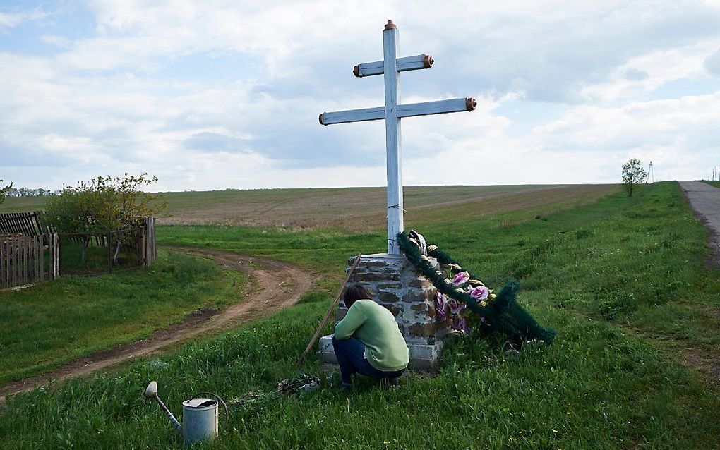 Een vrouw verzorgt het kruis bij de burnsite van vlucht MH17 van Malaysia Airlines. Rond de rampplek in Oost-Oekraine zijn veel van dit soort gedenktekenen te vinden. beeld ANP