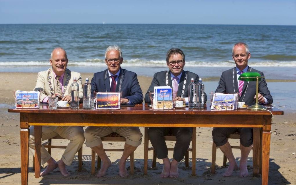 In vol ambtelijk ornaat schreven v.l.n.r. de burgemeesters Hoekema (Wassenaar),  Rijpstra (Noordwijk), Wienen (Katwijk) en Meijer (Zandvoort) op het strand in Noordwijk een groet vanaf de branding, bedoeld als protestbrief tegen de plaatsing van een ‘hekw