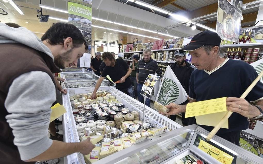 Boeren in het Zuid-Franse dorp Luc-la-Primaube plakken in een supermarkt proteststickers met de tekst ”Gemaakt van melk die met verlies is verkocht. Boeren gewurgd. Savencia (kaasfabrikant, red.) vetgemest.” beeld AFP