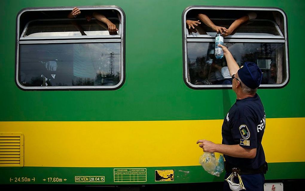 Een agent deelt flessen water uit aan vluchtelingen in de trein. beeld EPA