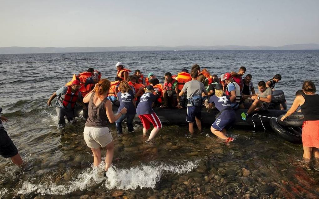 Vrijwilligers van Stichting Bootvluchteling, in blauwe poloshirts, helpen een groep bootvluchtelingen op Lesbos aan wal. beeld Jaco Klamer