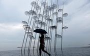 Een vrouw met paraplu passeert het kunstwerk “Umbrellas” van de Griekse architect Giorgos Zogolopoulos, aan de kust in Thessaloniki. beeld AFP