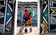 De Zuid-Afrikaanse kunstenares Esther Mahlangu (81) veegt de straat bij haar huis in Mabhoko Village. Haar kleurrijke werk wordt wereldwijd tentoongesteld, maar ze blijft vanuit haar woonplaats vechten voor de bedreigde Ndebele-cultuur. Beeld AFP