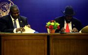 De president van Zuid-Sudan, Salva Kiir (r.) en rebellenleider Riek Machar tekenen het akkoord.  beeld AFP