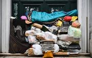 Een dakloze man slaapt op een stapel plastic zakken en kranten tegen een deur in de Italiaanse hoofdstad Rome. beeld AFP