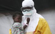 Een medewerker van Artsen zonder Grenzen in beschermende kleding houdt een kind vast dat vermoedelijk besmet is met ebola (Paynesville, Liberië). Beeld Getty Images