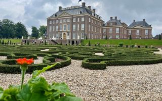Donkere lucht boven hoog gebouw. Ervoor hagen in krullerige vormen.