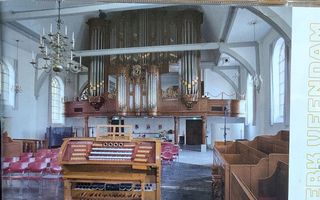 In een oude kerk staat op de kerkvloer de drieklaviers speeltafel van een orgel. Daarachter is het historische orgelfront te zien.