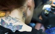 Een getatoëerde vrouw zet een tattoo bij een ander. beeld ANP, Lex van Lieshout