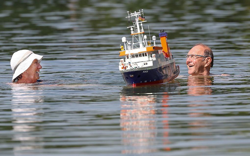 Ouderen zwemmen in een meer bij het Duitse Ertingen, terwijl een modelboot passeert. beeld AFP