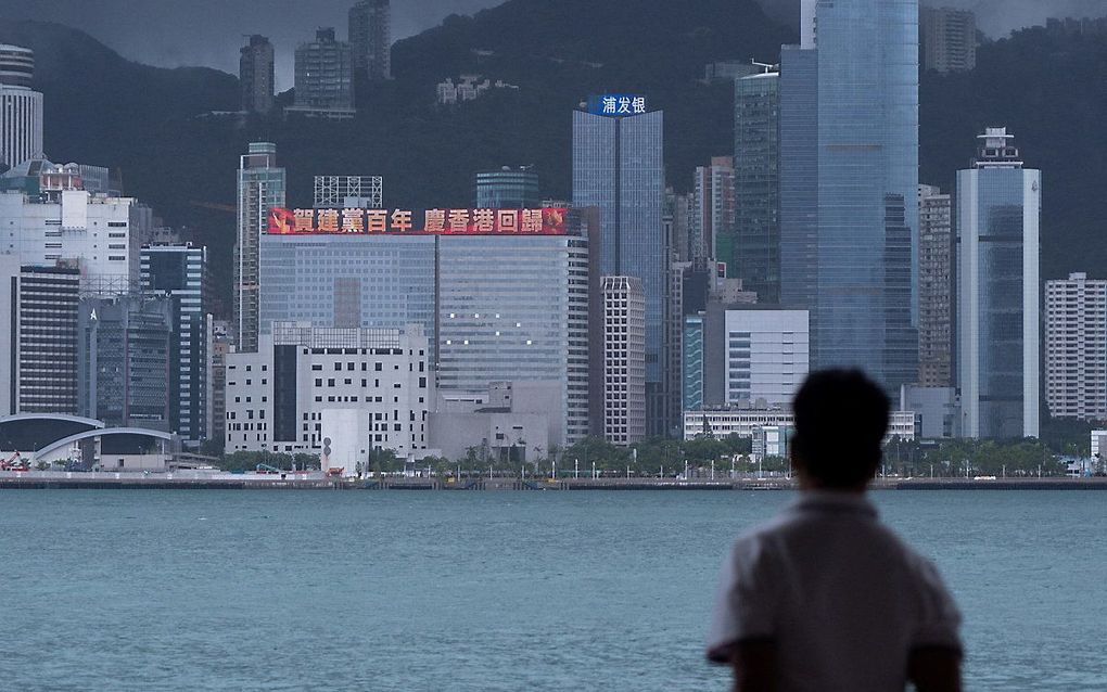 Een man kijkt naar een gebouw in Hongkong dat de honderdste verjaardag van de Chinese Communistische Partij herdenkt door middel van grote letters op de gevel. beeld AFP, Bertha Wang