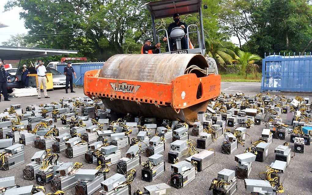 Politie in de Maleisische stad Miri rijdt met een stoomwals in beslag genomen machines waarop bitcoin gemined werd, plat. beeld AFP, Dennis Wong