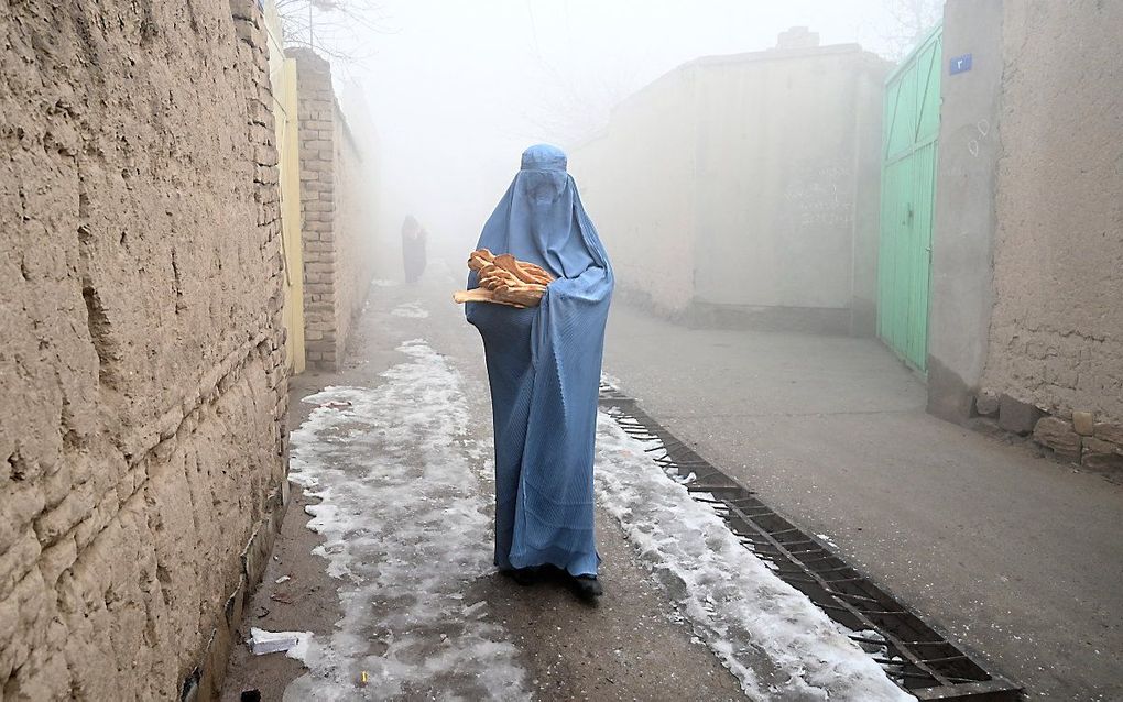 Een vrouw met een boerka loopt langs een weg naar haar huis nadat ze gratis brood heeft gekregen dat is uitgedeeld als onderdeel van de Save Afghans From Hunger-campagne in Kabul. beeld AFP, Wakil KOHSAR