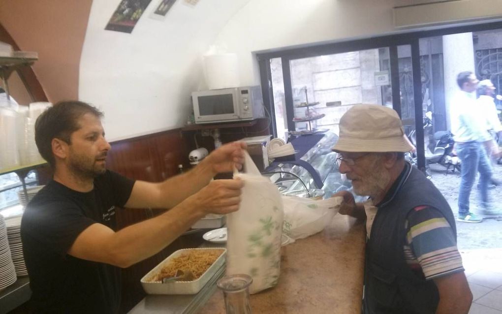 ROME. Eigenaar Francesco Botrugno (l.) van bar San Marcello in Rome geeft overgebleven voedsel aan een zwerver. beeld Ewout Kieckens