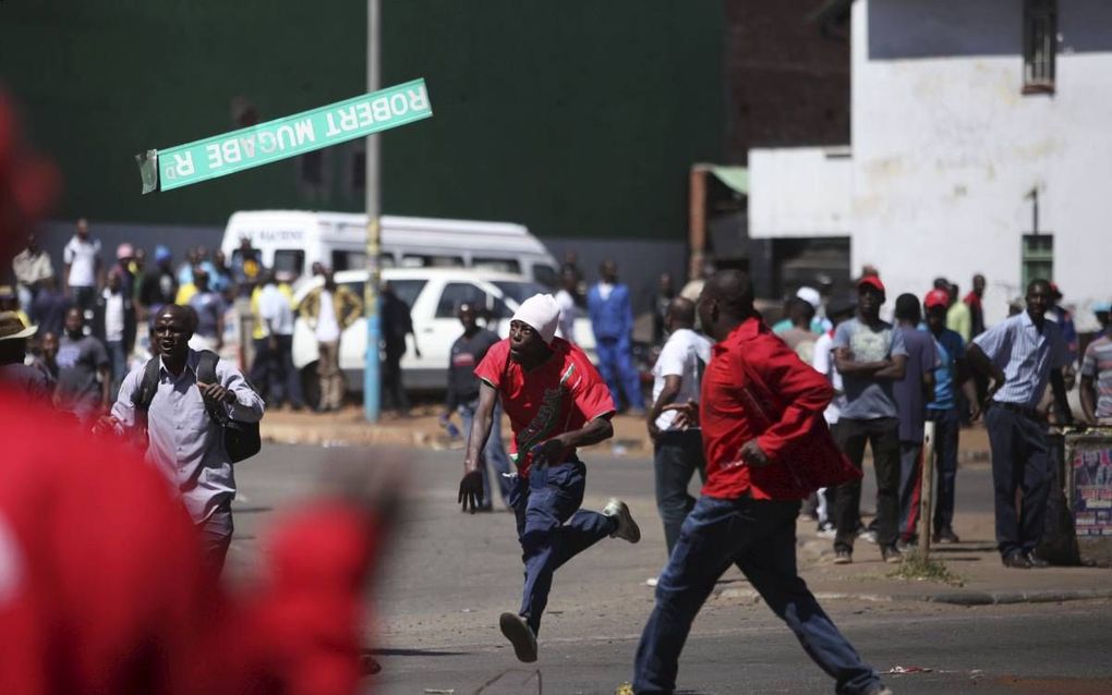 Een demonstrant smijt een straatnaambord met de naam van Robert Mugabe door de lucht tijdens protesten tegen de Zimbabwaanse president, eind augustus.  beeld AFP, Wilfred Kajese