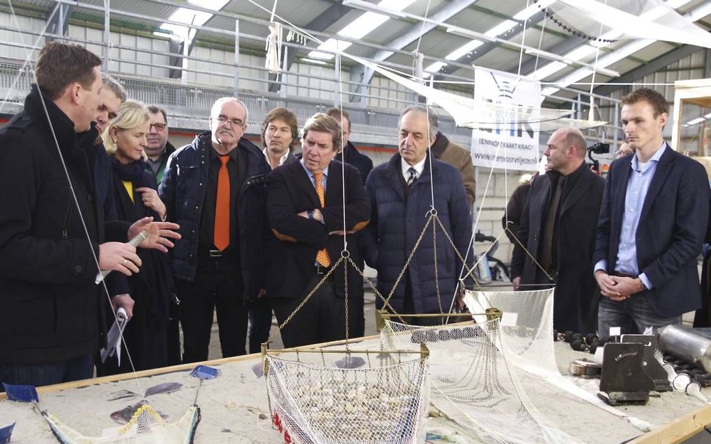 Johan Baaij (l), beheerder van het visserijinnovatiecentrum in Stellendam, geeft de Europarlementariërs uitleg over de verschillende visserijtechnieken. In het midden (armen over elkaar) de voorzitter van de visserijcommissie van het Europees Parlement, d