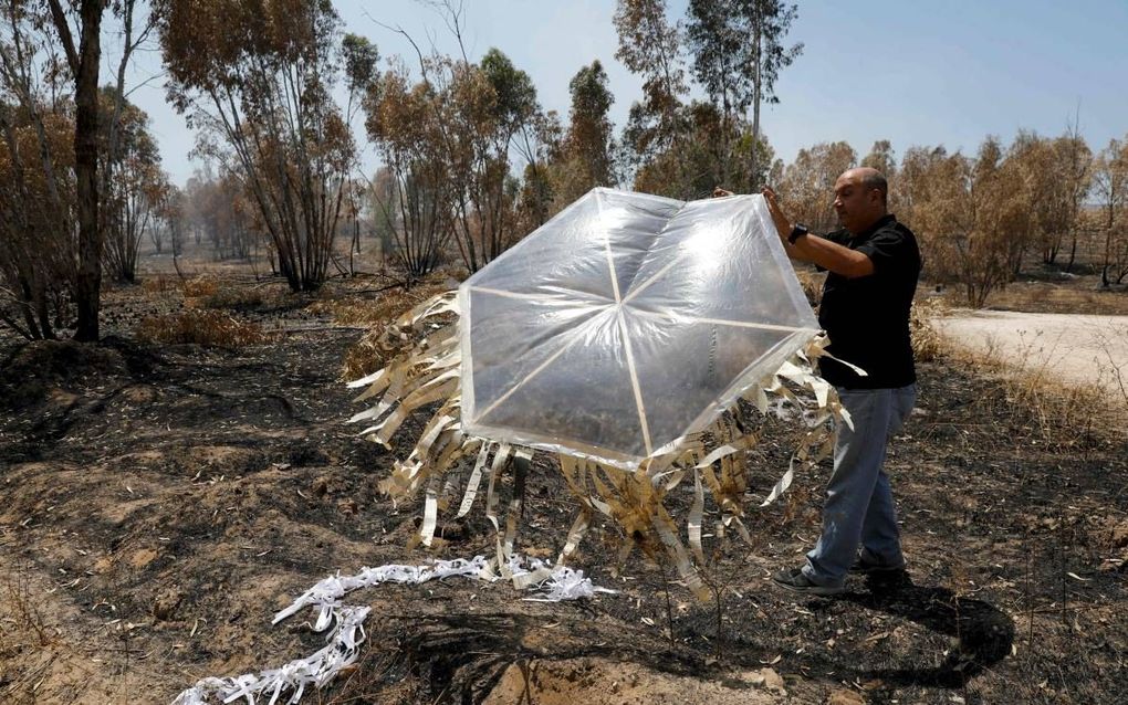 Een Israëlische brandweerman houdt een vlieger vast die dinsdag van Palestijnse zijde over de grens bij de Gazastrook is gekomen. De vliegers worden regelmatig uitgerust met molotovcocktails om zo veel mogelijk schade aan te richten. beeld AFP, Menahem Ka