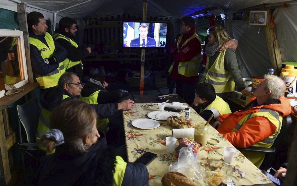 ‘Gele hesjes’ kijken maandagavond in Montabon, tussen Le Mans en Tours, naar de toespraak van president Macron. beeld AFP, Jean-Francois Monier