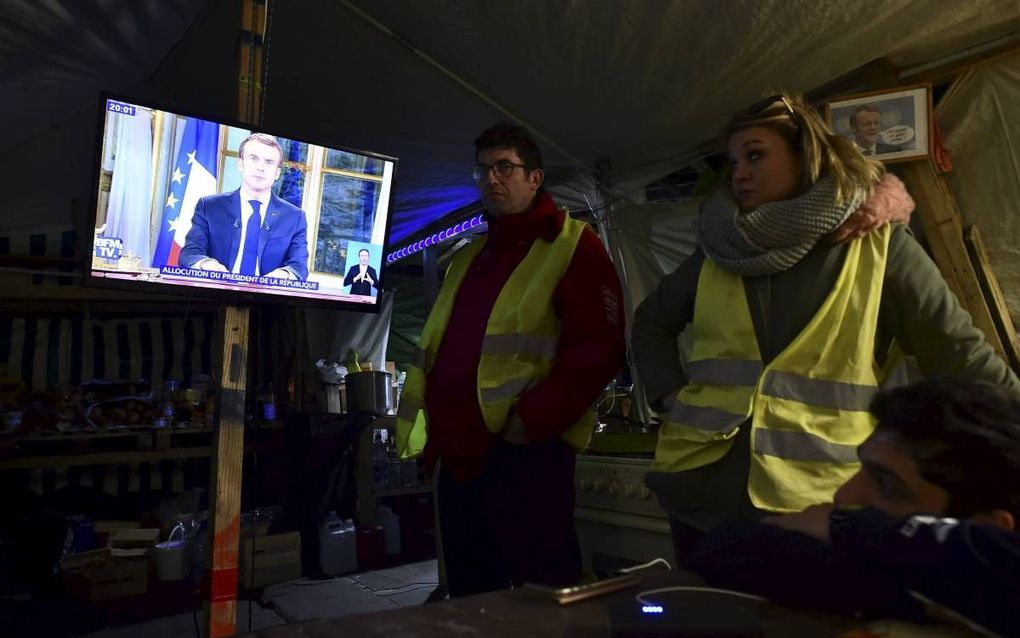 Twee in gele hesjes gestoken Fransen kijken maandag naar de tv-toespraak van president Macron. beeld AFP, Jean-Francois Monier