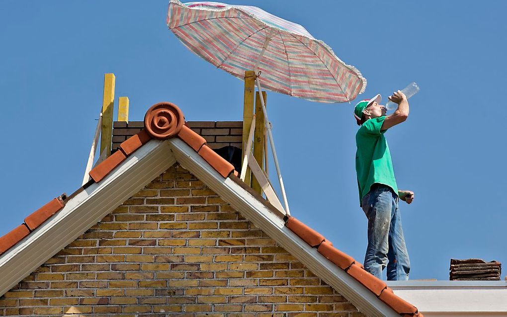 Een metselaar probeert tijdens zijn werkzaamheden op een dak met behulp van een parasol het hoofd koel te houden. beeld ANP