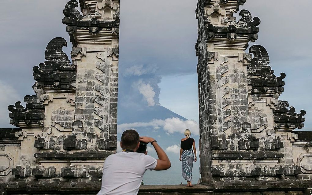 Toeristen poseren op Bali, terwijl op de achtergrond vulkaan Agung op uitbarsten staat. beeld EPA