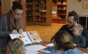 Kunstenaar Sabine Delhez wijst op plaatjes in het prentenboek waarover peuters en hun ouders een tekening maken tijdens het Mamacafé, een van de vele activiteiten in de bibliotheek van Veenendaal.