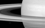 Maan Minas, linksonder in beeld, is maar een stipje vergeleken bij de planeet Saturnus en zijn ringen. Toch zou het maantje –396 kilometer in doorsnede– meer vaste stof bevatten dan de ringen. Die beslaan weliswaar een reusachtig oppervlak, maar blijken v