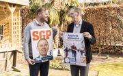 VVD’er Maarten van Panhuis (l.) en SGP-lijsttrekker Jan van Panhuis houden elkaars verkiezingsposter vast. Vader en zoon voeren beide campagne voor een raadszetel in Harderwijk. beeld André Dorst