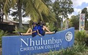 Sophie en Jesse de Zwart uit Nederland op het naambord van het Christian College in Nhulunbuy, in Noord-Australië. Ze moesten wennen aan het dragen van de verplichte hoed. beeld Esther de Zwart