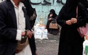 Een Jemenitische vrouw (m.) zit naast het voedselrantsoen dat ze heeft gekregen van een hulporganisatie. beeld EPA, Yahya Arhab