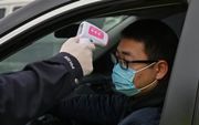 Een agent meet de lichaamstemperatuur van een automobilist in een buitenwijk van Wuhan. beeld AFP