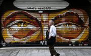 Een man loopt langs een gesloten winkel in Athene. Beeld EPA