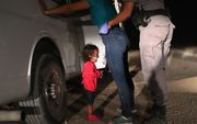 Een vrouwelijke vluchteling wordt aan de grens tussen Mexico en de VS opgepakt en onderzocht, terwijl haar dochtertje staat te huilen. beeld AFP