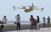Mensen kijken naar een blusvliegtuig die water gaat scheppen op Gran Canaria. beeld EPA