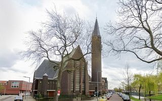 Kerkgebouw met toren op de hoek van een straat. Langs de weg staan auto’s geparkeerd.