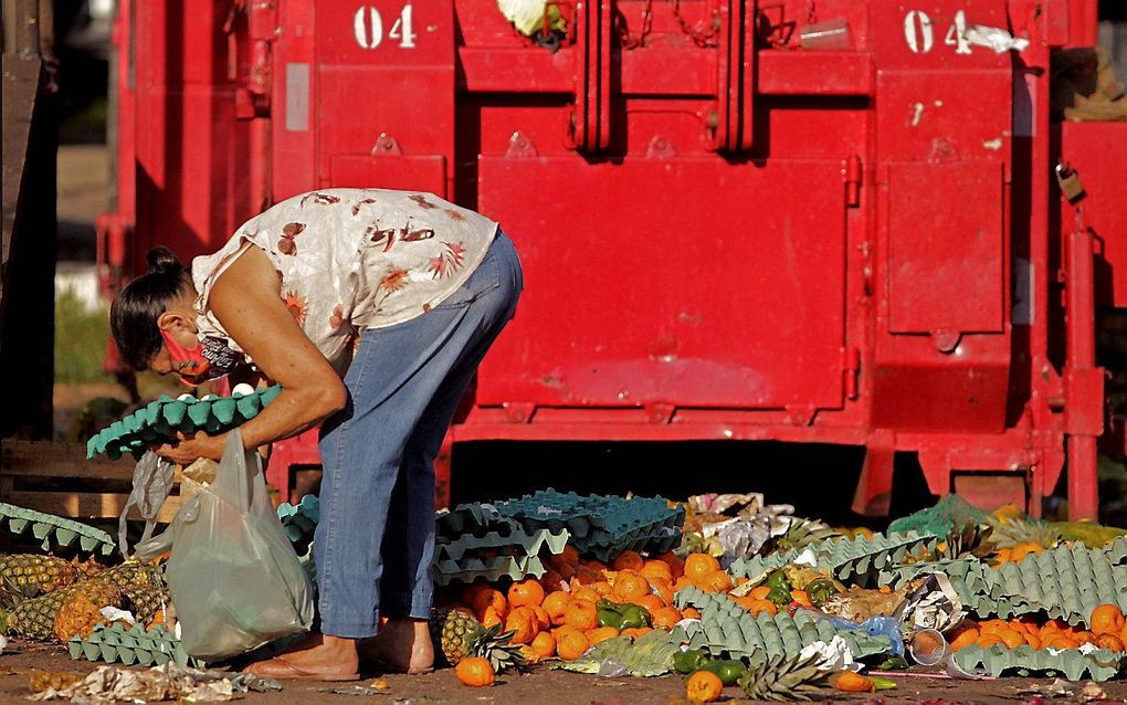 Een vrouw in Belem, Brazilië, zoekt naar voedsel bij een afvalcontainer. Beeld AFP, Raimundo Pacco