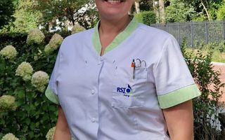 Verpleegkundige in witte werkkleding met bomen op de achtergrond