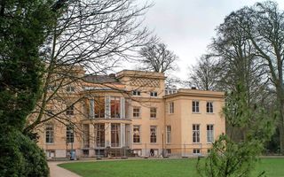 Een gekleurd gebouw met grote ramen aan een groot grasveld bij een vijver.