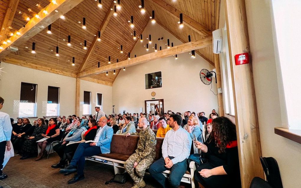 Interieur van een kerkgebouw gevuld met banken die vol zitten met mensen.