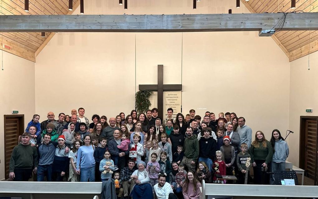 Voorin een kerkgebouw poseert een grote groep mensen. Achter hen tegen de muur een kruis.