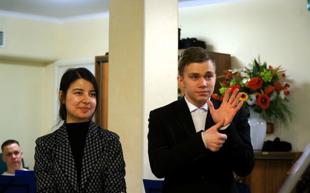 Jonge vrouw staat met haar man voor in de kerk in gebarentaal te getuigen.  